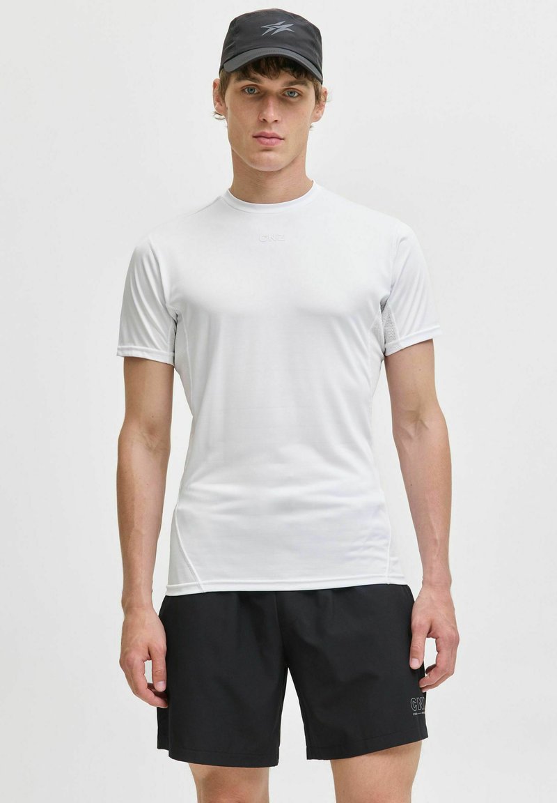 Vit sportt-shirt med korta ärmar, slät textur och en logo på bröstet, i kombination med svarta shorts som har en liten logo.