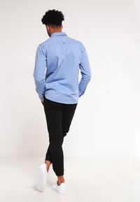 Světle modrá košile s dlouhým rukávem, s límečkem na knoflíky, s jemnou texturou, spárovaná s černými slim-fit kalhotami a bílými teniskami.
