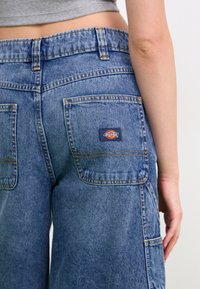 Pantalones cargo de denim azul con una cintura alta, dos bolsillos traseros, costuras visibles y un parche de marca en el bolsillo derecho.