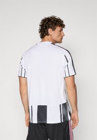 T-shirt de sport blanc avec des rayures verticales noires et grises sur les manches et l'ourlet. Tissu léger et respirant, design à col rond.