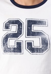 White cotton t-shirt with a navy blue ringer collar featuring a distressed graphic of the number "25" in a bold font.