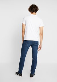 Vit kortärmad T-shirt kombinerad med blå denimjeans. Jeansen har en slim fit och en medelvatten. Svarta sneakers fulländar outfiten.