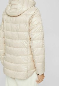 Chaqueta de plumas de color beige claro con un diseño texturizado y acolchado, capucha y un acabado ligeramente brillante. Sin hardware ni acentos visibles.