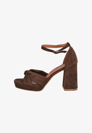 Tacones plataforma de ante marrón con detalle de nudo en la parte frontal y una correa al tobillo. Tacón ancho y grueso para mayor estabilidad. Forro interior suave.