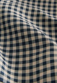 Textilie s kostkovaným vzorem v námořnicky modré a béžové barvě. Látka působí měkce a má texturované tkaní.