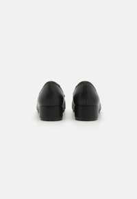 Svarta läderskor med en slät yta, låg blockklack, rund tå och minimalistisk design. Inga synliga mönster eller hårdvarudetaljer.