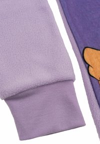 Manica in pile viola con polsino a coste accanto a una sezione di tessuto viola che presenta parte di un design di un personaggio dei cartoni animati arancione.