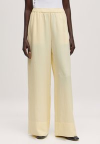 Wijde beenbroek in lichtgele stof. Heeft een elastische tailleband en een gladde textuur, met een losse pasvorm en subtiele glans.