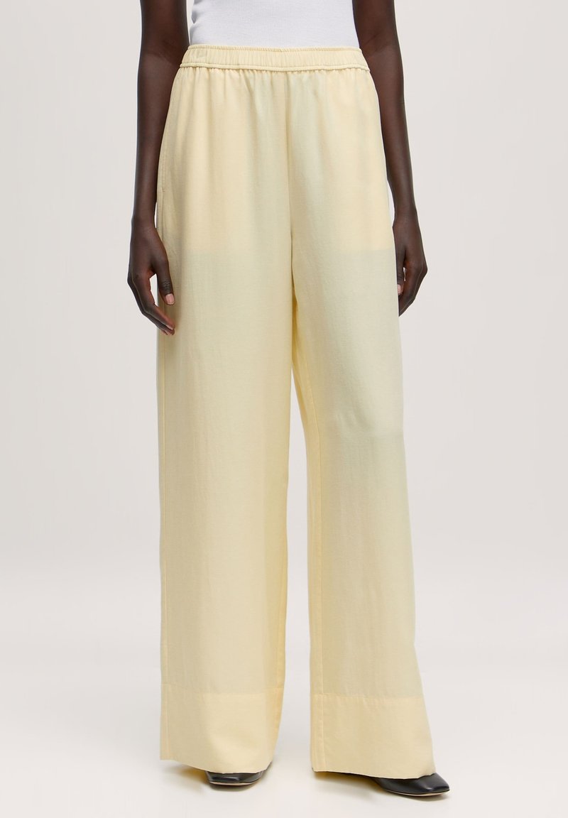 Wijde beenbroek in lichtgele stof. Heeft een elastische tailleband en een gladde textuur, met een losse pasvorm en subtiele glans.