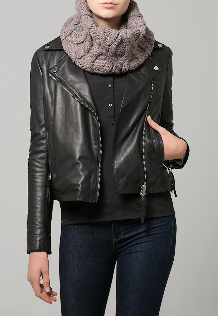 Personne portant une veste en cuir noire, une chemise noire, un jean bleu foncé et une écharpe taupe épaisse en tricot, avec une main dans la poche de la veste.