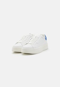 Hvit sneakers med overdel i glatt lær, flate snøringer, en blå detalj ved hælen og en tykk hvit såle. Minimal merking synlig.