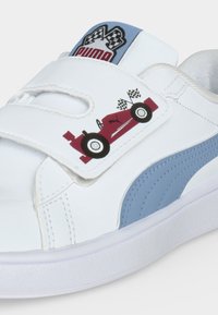 Λευκό αθλητικό παπούτσι Puma με μπλε ρίγα, με γραφικό κόκκινου αγωνιστικού αυτοκινήτου και καρό σημαίας στο λουράκι με βέλκρο και λογότυπο στη γλώσσα.