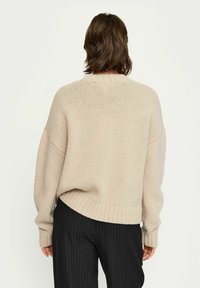 Beige gestrickter Pullover mit lockerer Passform, gerippten Bündchen und Saum. Kombiniert mit schwarzen Nadelstreifen-Hosen, die eine lässige Silhouette zeigen.