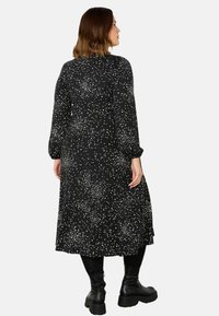 Černé šaty s náhodným vzorem bílých teček, dlouhými rukávy a střední délkou, doplněné černými robustními botami.