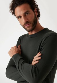 Dunkelgrüner Pullover mit langen Ärmeln und rundem Ausschnitt. Weiche Textur, taillierte Bündchen und ein sauberes, minimalistisches Design. Keine sichtbaren Muster.