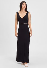 Black maxi dress with a V-neck, sleeveless design, textured cut-out waist detail, and a fitted silhouette. Worn with light-colored shoes.