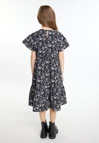 Zwarte bloemenjurk met korte, brede mouwen, met paarse en witte bloemen, gelaagde rok en een knoopsluiting op de rug. Gediend met zwarte laarzen.