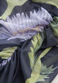 Tekstuuriga kangas, mis sisaldab rohelise ja lillaka lillemustriga segu tumedal taustal, kogutud servadega ja kerge võrgusilmast.