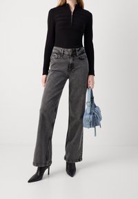 Schwarzer Reißverschluss-Top mit gerippter Textur, hoch taillierte graue Denim-Weitbein-Jeans, schwarze spitze Absätze und eine hellblaue Handtasche.