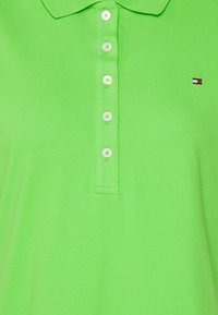 Zelené polo tričko s texturovanou tkaninou. Obsahuje klasický límec, šest knoflíků a malé logo na levé hrudi.