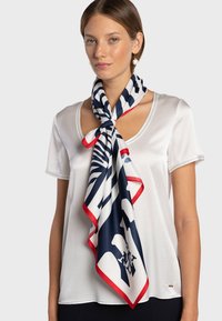 Foulard en soie motif rayé bleu marine et blanc avec bordure rouge, porté autour du cou d'un mannequin vêtu d'un t-shirt blanc.