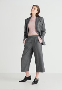 Sivi volneni sako z izrezanimi reverji, kombiniran s roza rebrastim topom in sivimi skrajšanimi hlačami. Črne gležnjarje dopolnjujejo outfit.