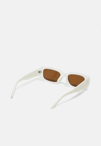 Baltas taisnstūra formas saulesbrilles ar brūniem lēcas tonējumā, piedāvājot elastīgu rāmi un gludas rokas modernam dizainam.