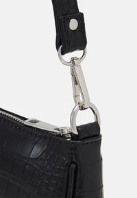 Zwarte nep krokodillenleren handtas hoek met zilveren rits en afneembare strap sluiting tegen een witte achtergrond.