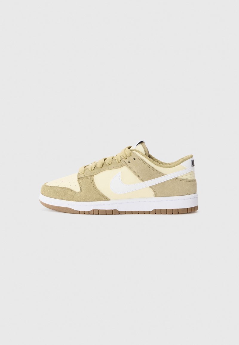Basket basse Nike beige et crème avec logo swoosh blanc et semelle en gomme, vue de côté sur un fond uni.