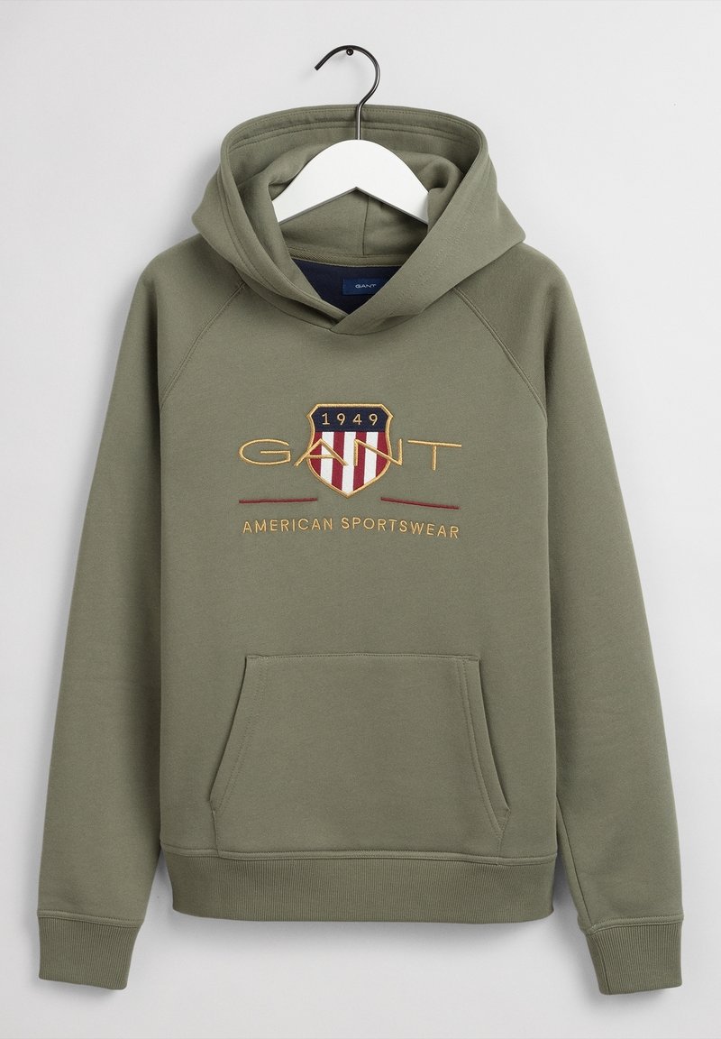Sweat à capuche vert olive avec poche avant, logo écusson brodé GANT, texte "1949" et "American Sportswear", présenté sur un cintre blanc.