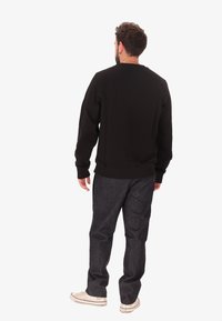 Felpa nera con polsini e orlo a coste, abbinata a jeans scuri e sneakers bianche. La vista mostra la parte posteriore dell'outfit.