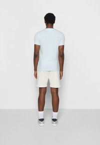 Hellblaues Kurzarmhemd mit Rundhalsausschnitt, kombiniert mit cremefarbenen Shorts und weißen Socken. Sportschuhe mit navyblauen und grauen Akzenten.