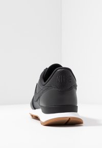 Svart lädersportskor med texturerade accenter, vit mellansula och yttersula av gummigummi. Har ett präglat logotyp på hälen.