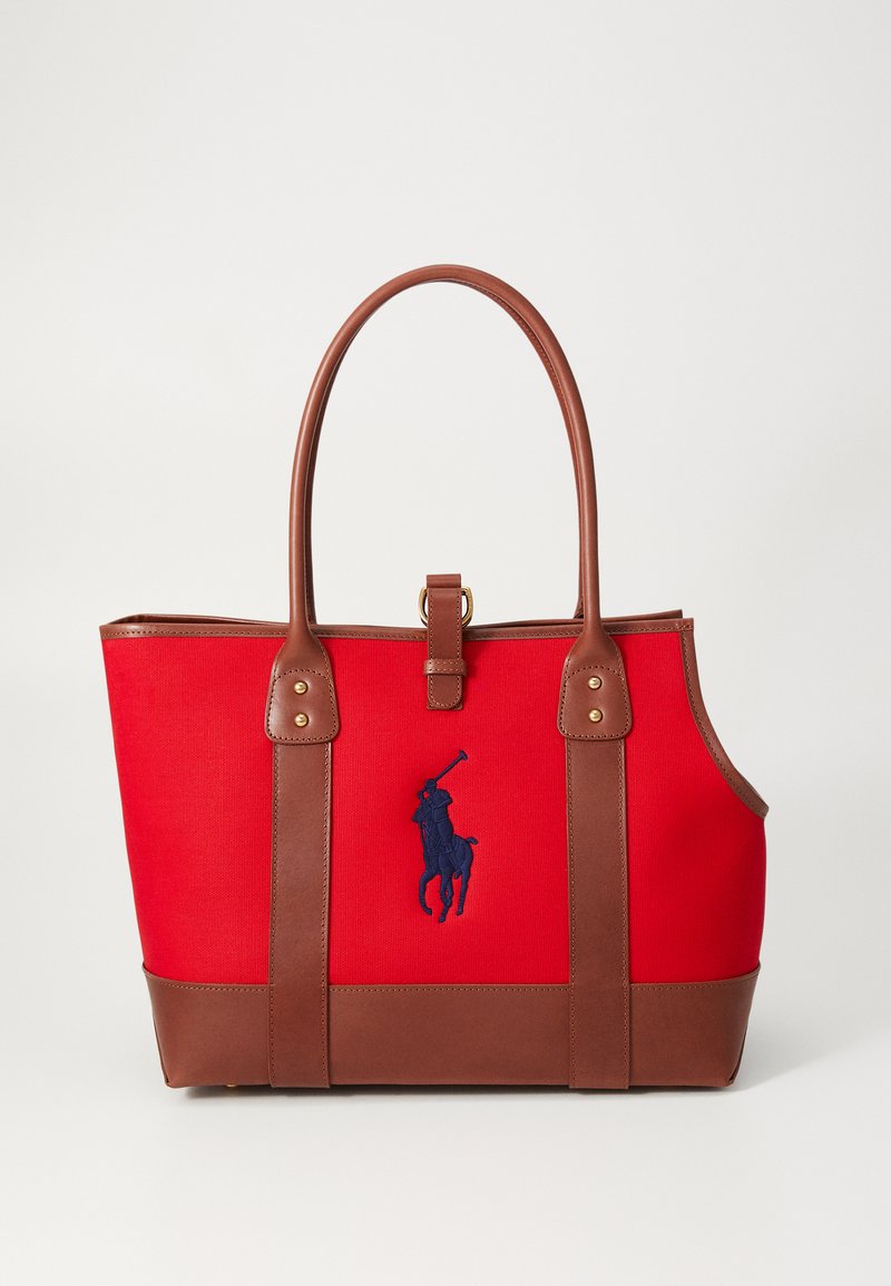 Saco de lona vermelho com detalhes em couro castanho, duas alças, ferragens douradas e logótipo bordado em azul-marinho de um jogador de polo.