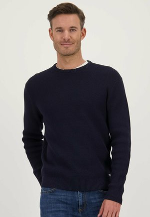 Marineblauwe gebreide trui met textuur, ronde halslijn en geribde boorden en zoom, gedragen over een wit shirt. Casual pasvorm en veelzijdig ontwerp.