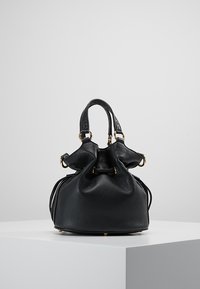 Sac seau en cuir noir avec une finition texturée, un haut resserré, des poignées doubles et des accents en métal doré. Base robuste avec quatre pieds de protection.