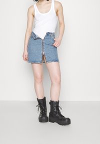 Jeanskjol med blixtlås fram och sidofickor, ljusblå färg, i kombination med svarta snörstövlar med platå. Vit linne bärs.