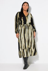 Lange, gestreepte jurk met een v-hals, voorzien van zwarte en beige strepen. Touwtjes in de taille en lange mouwen, gecombineerd met zwarte laarzen.