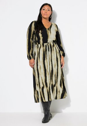 Lange, gestreepte jurk met een v-hals, voorzien van zwarte en beige strepen. Touwtjes in de taille en lange mouwen, gecombineerd met zwarte laarzen.