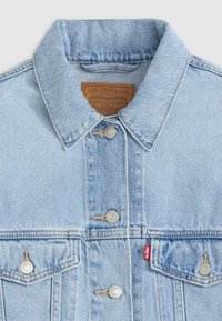Veste en denim bleu clair avec un col classique, des boutons en métal argenté, deux poches poitrine à l'avant et une étiquette en cuir dans le cou.