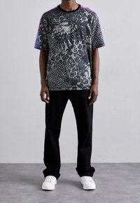 Svart mönstrad t-shirt med kort ärm med leopard- och ormdesign, med färgglada detaljer på axlarna, i kombination med svarta byxor och vita sneakers.