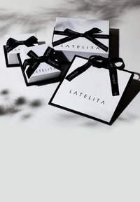 Białe pudełka na prezenty z czarną wstążką, z logo "LATELITA". Pudełka różnią się rozmiarem, mają kontrastowe czarne krawędzie i kokardy.