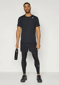 Ropa deportiva negra de Nike que consiste en una camiseta ajustada de manga corta, pantalones cortos y leggings largos, complementada con una botella de agua negra y zapatillas.