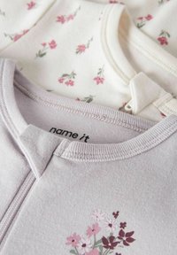 Kaks pehmet puuvillast beebikeha rõivast: üks helelilla lillemustriga ja üks beež väikeste roosade lilledega. Mõlemal on ümar kaelus.