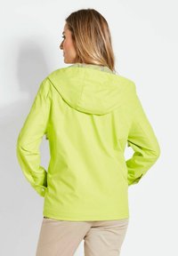 Helle limettengrüne wasserdichte Jacke mit Kapuze, elastischen Bündchen und glatter Textur. Sie verfügt über Reflektoren im Halsbereich.