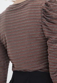 Brun randig topp med en strukturerad mönster, med puffärmar och ribbade detaljer. Materialet verkar vara lätt och elastiskt.