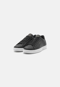 Mustad nahast sneakersid sileda pinnaga, valge kummist tallaga ja mustade paeltega. Kuldne logo aktsent keelega. Klassikaline madala pära disain.