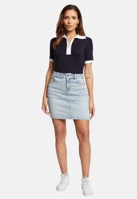 Polo shirt bleu marine avec col blanc, assorti à une jupe en denim clair. Les chaussures comprennent des baskets blanches. Design de tenue simple et décontractée.