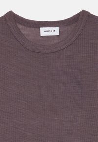 Ribbete, mauve skjorte med rund hals. Har en merkelapp som sier "name it." Myk tekstur og lett stoff er tydelig.