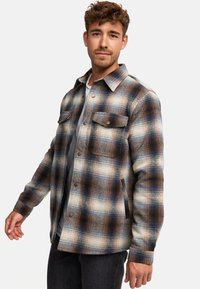 Giacca in flanella a quadri nei colori blu, marrone e crema con due tasche sul petto, chiusura con bottoni e tessuto strutturato.